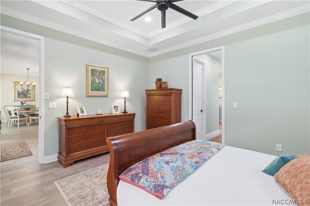 PRIMARY BEDROOM  Another view highlights the generous size of the primary suite, beautiful tray ceiling w/ layered crown molding, modern ceiling fan & porcelain tile flooring. Wide doorways provide easy access to the adjoining living area & private bath.