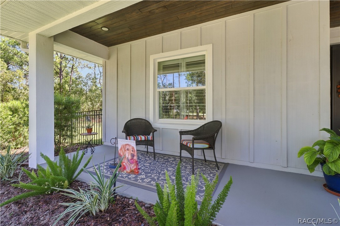 COVERED FRONT PORCH  A cozy sitting area under the covered porch features a rich wood plank ceiling, recessed lighting, landscaped greenery & views across the property.