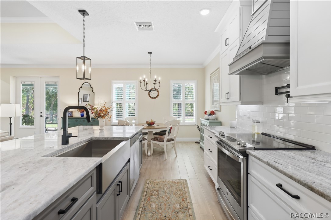 KITCHEN DETAIL  Crisp white cabinetry, subway-tile backsplash, stainless range, statement vent hood, pot filler, expansive counters & a large island create a polished, functional workspace.