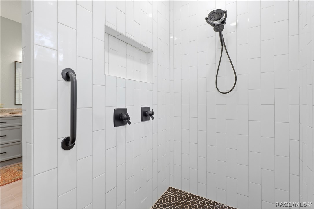 WALK-IN TILED SHOWER  Gorgeous walk-in shower is finished from floor to ceiling in crisp white tile w/ contrasting dark hexagon tile flooring, built-in recessed niche, grab bar & handheld showerhead. Matte-black fixtures give the space a sharp, modern finish.