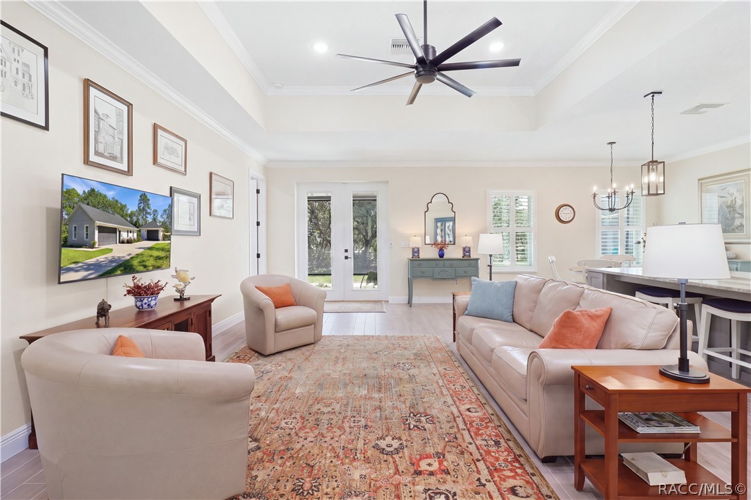 GREAT ROOM VIEW  Airy living space w/ tray ceiling, crown molding, modern ceiling fan, abundant natural light & French-style glass doors opening toward the outdoor living area.