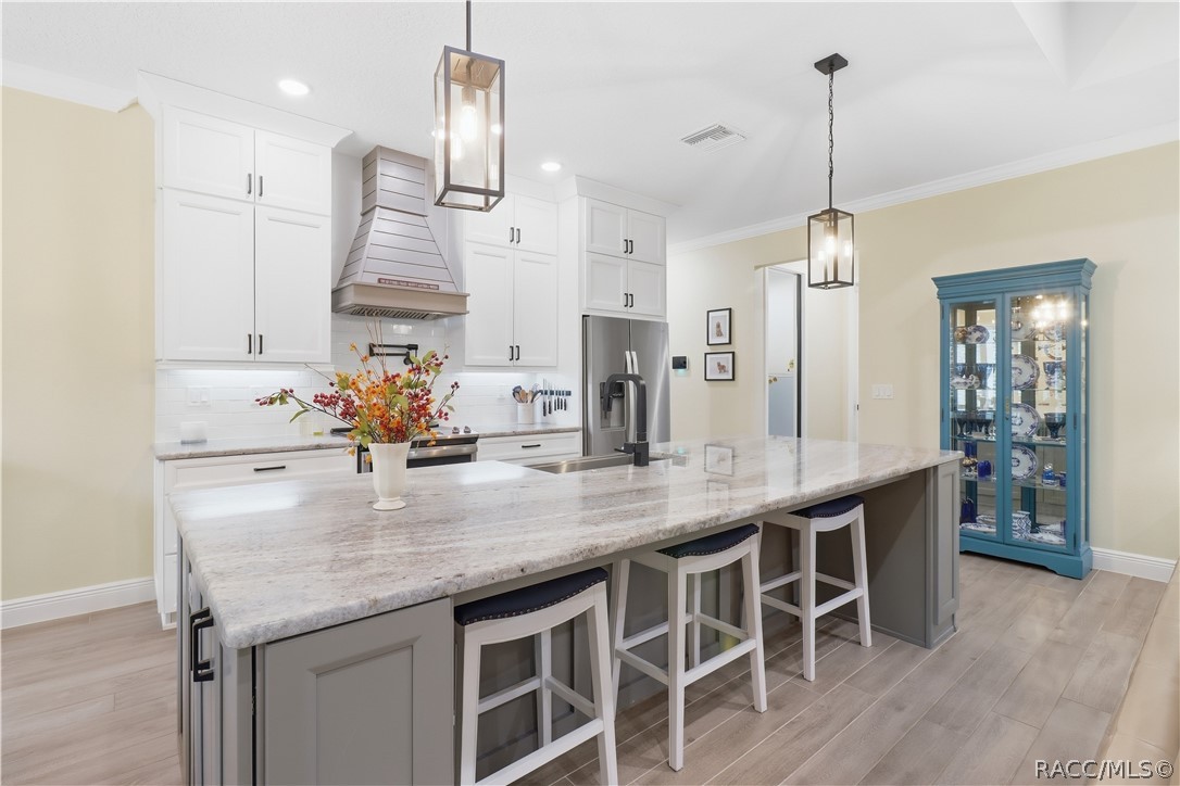 ENTERTAINER'S KITCHEN  Extra-large island offers abundant seating, prep & serving space while tall cabinetry, stainless appliances, statement hood, pendant lighting & open sightlines elevate the room.