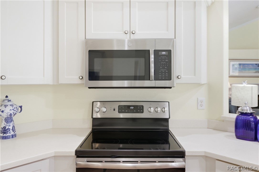Kitchen Appliances  NEWER Stainless-steel electric range & built-in microwave surrounded by white cabinetry and corian countertops.