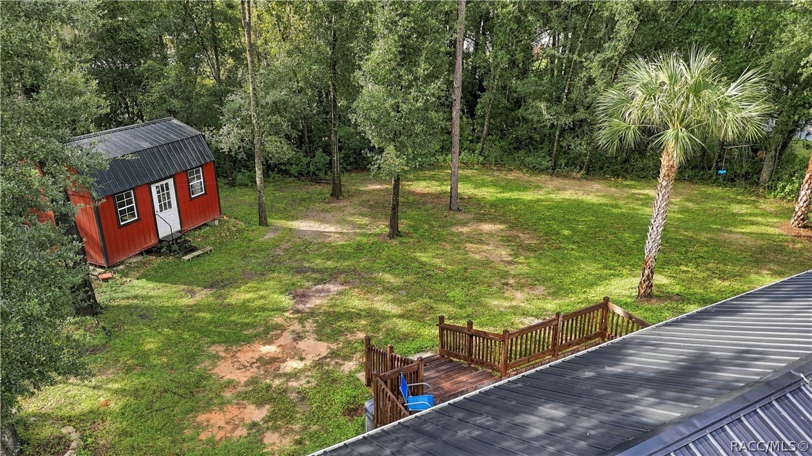 Aerial Backyard View  Enjoy the generous green space, mature shade trees, rear wooden deck & attractive red storage building that adds character to this inviting property.