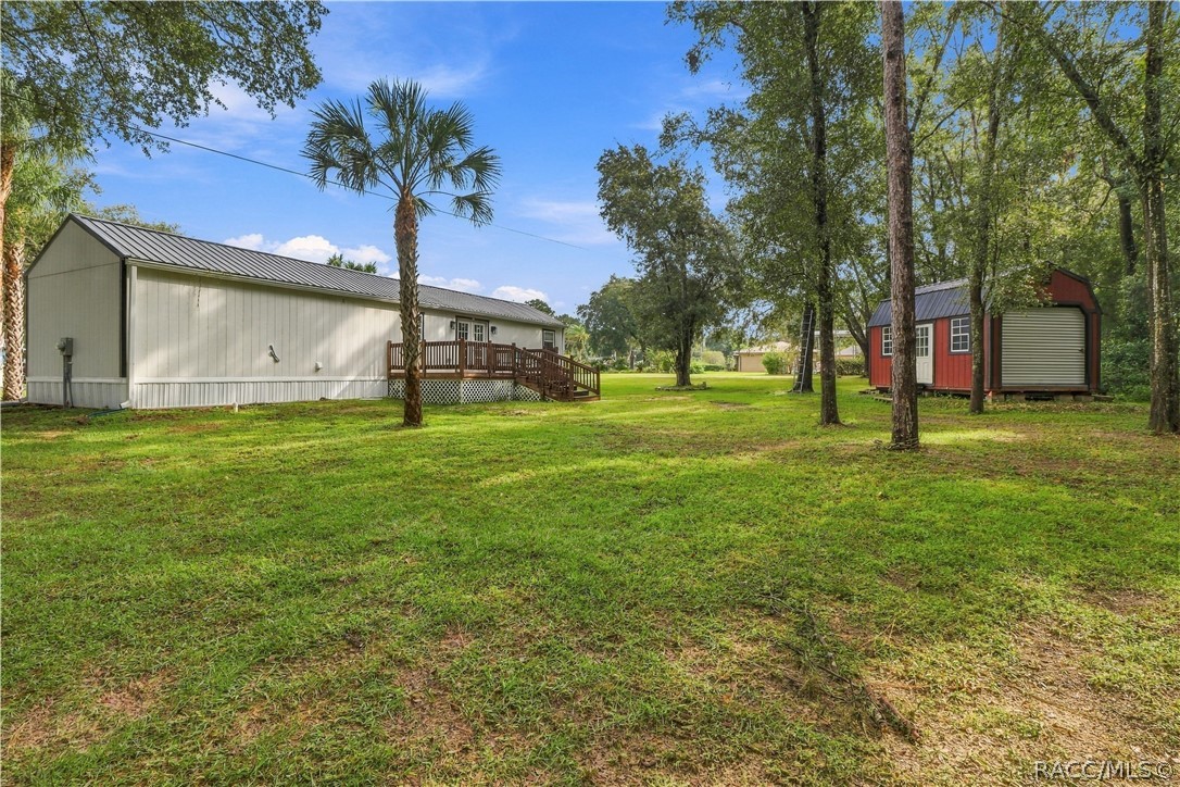 Backyard & Storage Building  Spacious backyard featuring mature trees, open lawn, wooden deck & a distinctive RED DETACHED STORAGE BUILDING w/metal roof & roll-up door.