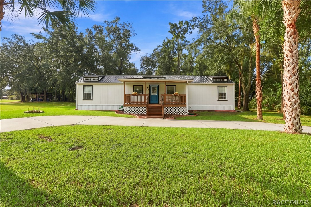 Charming Front Exterior  Beautifully presented home featuring a METAL ROOF, inviting COVERED FRONT PORCH, attractive landscaping & a welcoming blue front door.