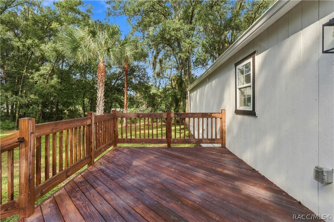 Rear Deck  Spacious wooden deck featuring sturdy railings & room for outdoor seating, surrounded by Florida greenery & mature palms.