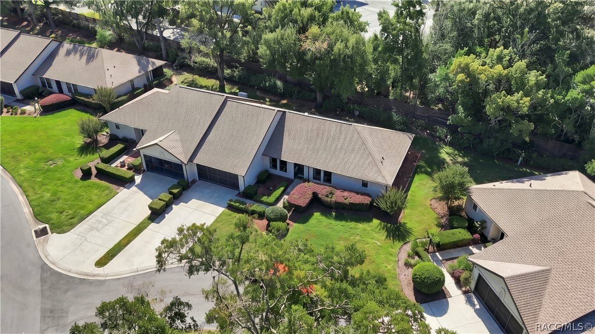 Aerial perspective showcasing the home's roofline, beautifully maintained grounds, surrounding residential properties, and wooded backdrop.