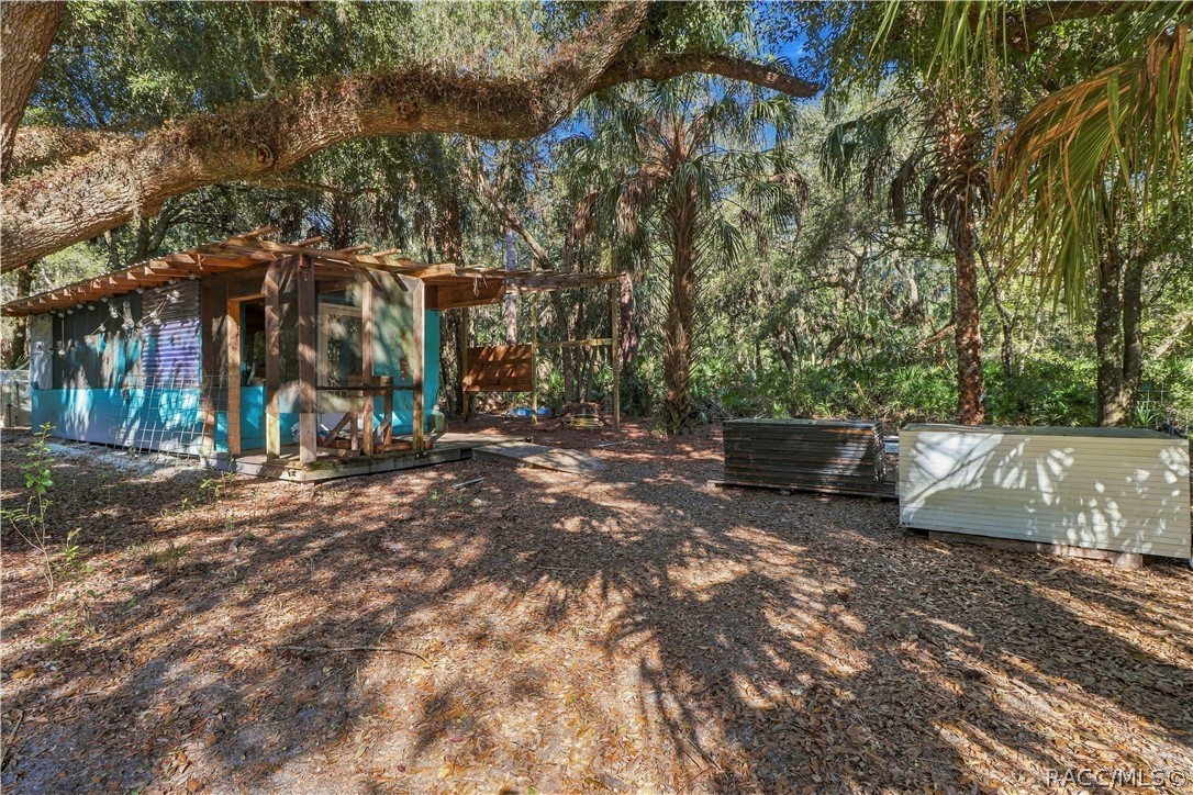 COUNTRY CHARACTER & OUTDOOR POSSIBILITIES! This rustic outbuilding features a covered wooden porch & adjoining open-air structure beneath the shade of mature trees.