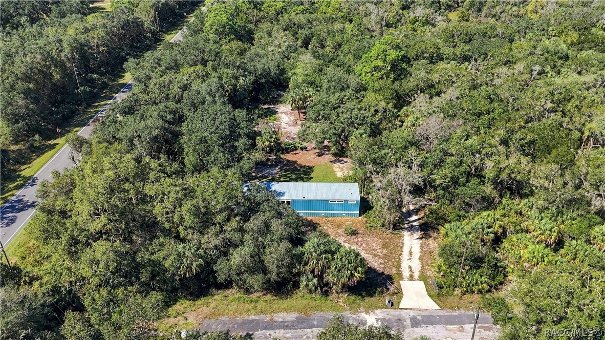 A BIRD'S-EYE VIEW! An aerial perspective showcases the home's wooded surroundings, natural landscape & driveway leading to the property.