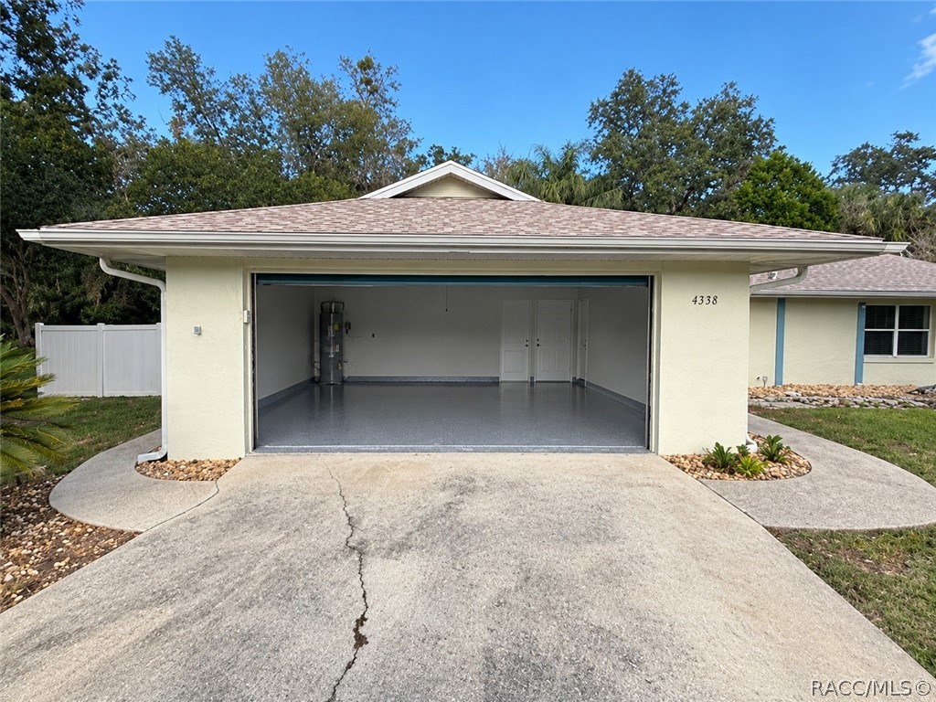 Clean, empty garage interior: smooth grey painted concrete floor, a white sectional garage door with metal rails and a garage door opener, a fluorescent tube light, a textured ceiling, beige walls, and a light wood empty shelving unit with two bays and four shelves against the back wall. No mower, boxes or clutter in this shot  this is a different, newer garage photo than the two cluttered garage shots in the old set.