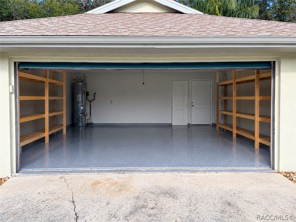 Clean, empty garage interior: smooth grey painted concrete floor, a white sectional garage door with metal rails and a garage door opener, a fluorescent tube light, a textured ceiling, beige walls, and a light wood empty shelving unit with two bays and four shelves against the back wall. No mower, boxes or clutter in this shot  this is a different, newer garage photo than the two cluttered garage shots in the old set.