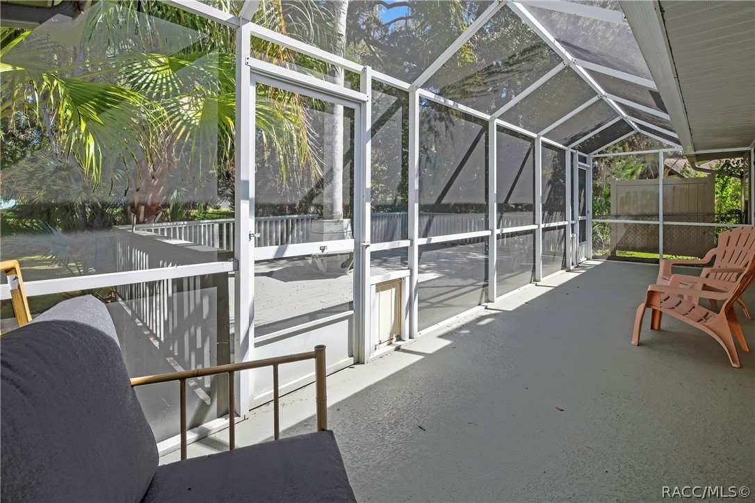 Wood deck: grey wood deck planks, railing, a built-in bench around a palm tree trunk, steps down to a fenced lawn, palm trees, oaks with Spanish moss, and a chain-link fence in the background.