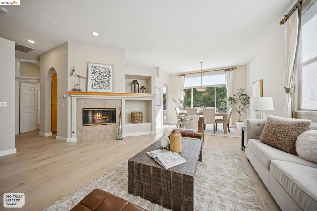 Living area featuring wood-finish flooring, a tile-surround fireplace, built-in shelving, arched doorway detailing, and recessed lighting