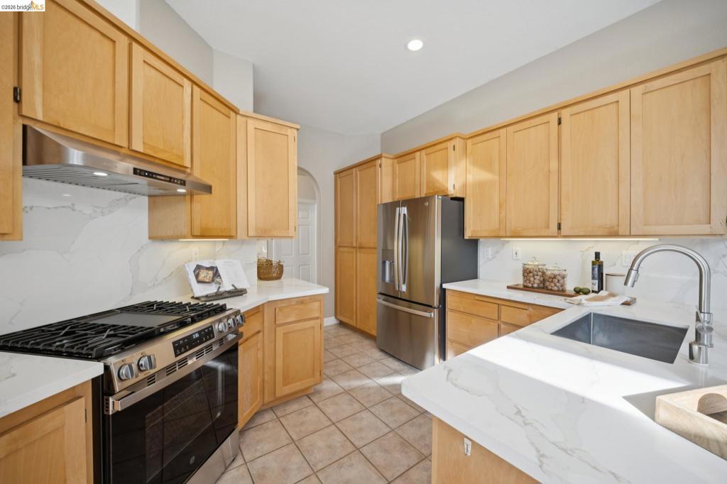 Kitchen featuring light wood cabinetry, quartz countertops, a full-height stone-pattern backsplash, stainless steel appliances, and a stainless steel undermount sink with a gooseneck faucet