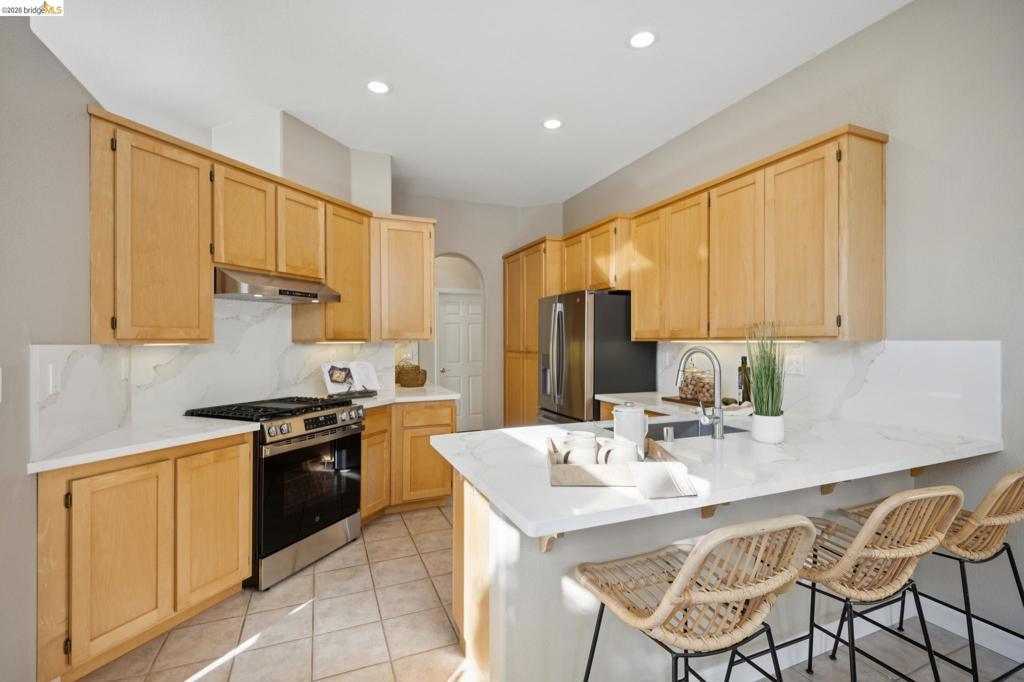 Kitchen featuring light wood cabinetry, white stone-finish countertops, stainless steel appliances, a tile backsplash, and recessed lighting