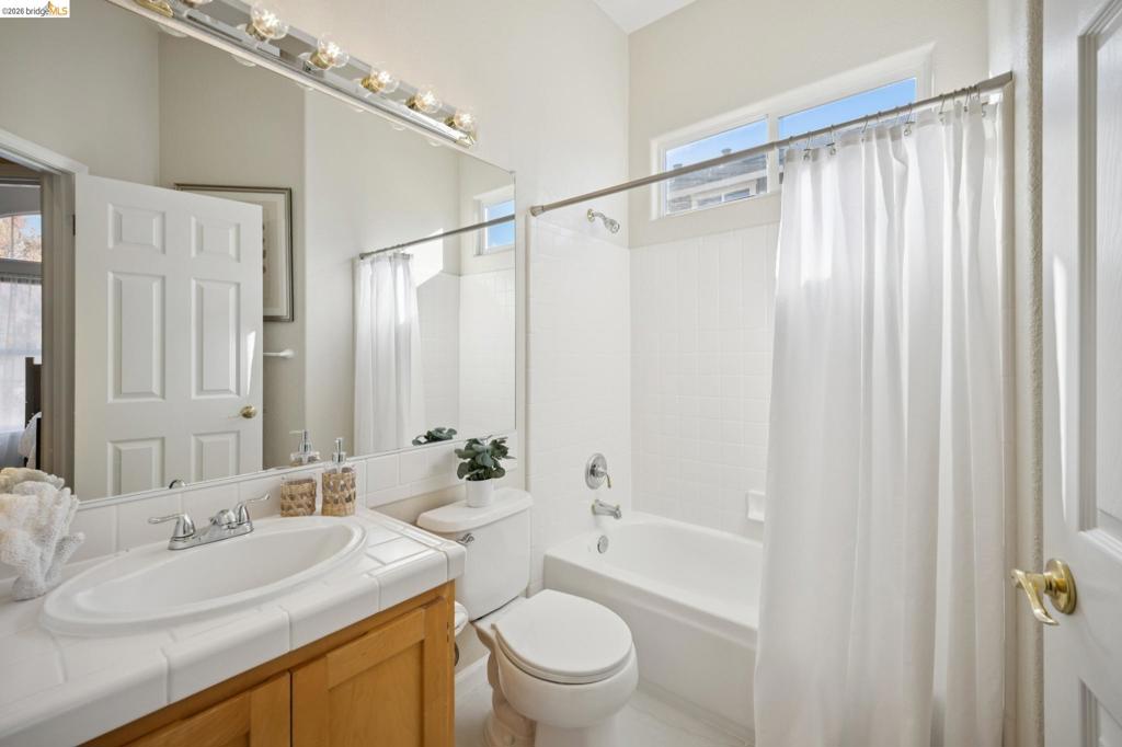 Bathroom featuring a tile-surround vanity, wooden cabinetry, a full-width wall mirror, and a tub-shower combination with tile surround and clerestory window