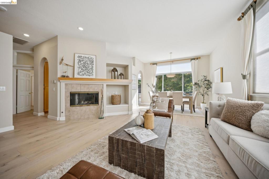 Open-concept living area featuring wood-finish flooring, recessed lighting, arched doorways, a tile-surround fireplace with a wood mantel, and built-in display shelving