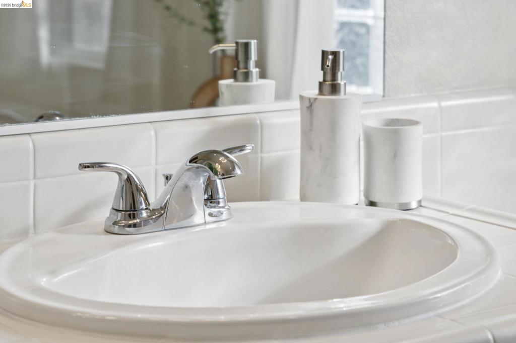 Inset porcelain sink with polished chrome double-handle faucet, integrated tile countertop, and flat-panel wall mirror