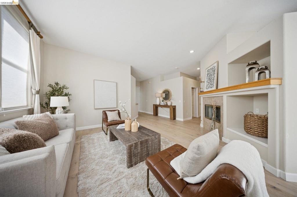 Living space featuring vaulted ceilings, light-toned wood-finish flooring, a tile-surround fireplace, and built-in shelving with wood mantel detailing