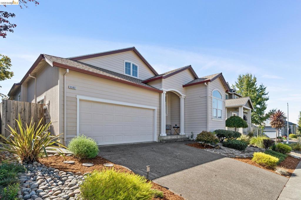 Exterior featuring horizontal lap siding, an arched entryway with column detailing, a multi-gabled roofline, an attached two-car garage, and landscaped rock garden beds