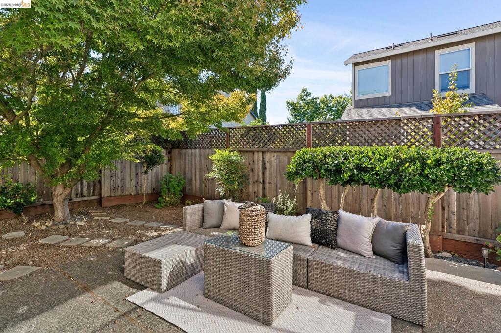 Rear courtyard featuring a concrete patio, decorative wood lattice fencing, mature tree canopy, and stone pavers