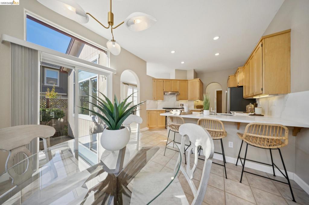 Open-concept kitchen featuring light wood cabinetry, white countertops, ceramic tile flooring, a multi-arm brass chandelier, and a sliding glass door with a transom window