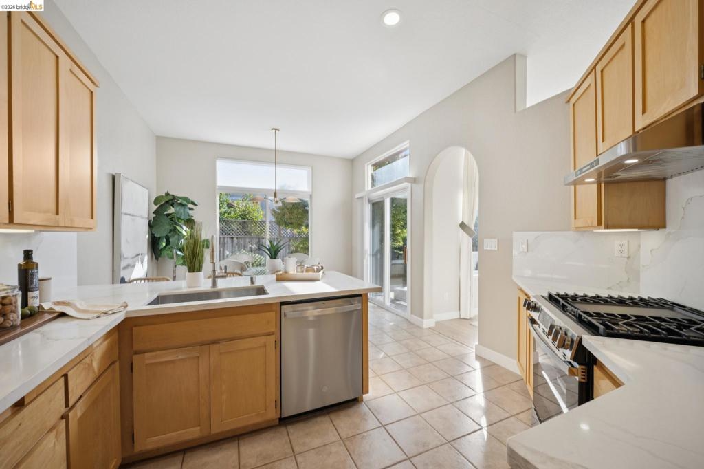 Kitchen featuring light wood cabinetry, white stone countertops, tile flooring, stainless steel appliances, and a prominent arched entryway