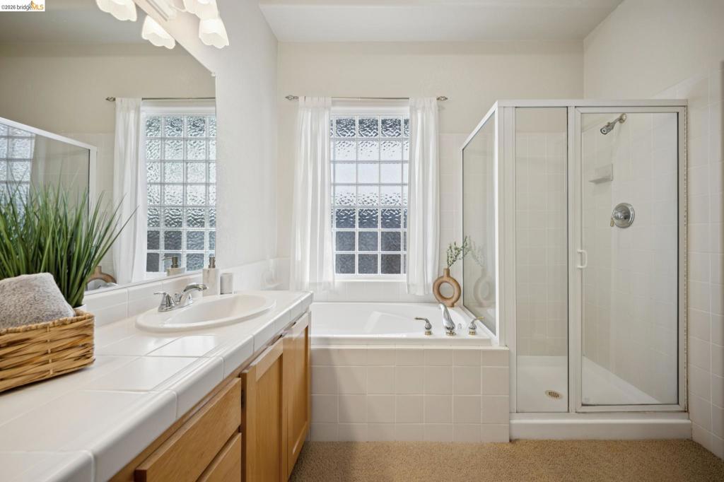 Bathroom featuring a tile-surround soaking tub, a glass-enclosed shower stall, a vanity with an integrated sink, and an expansive wall-mounted mirror