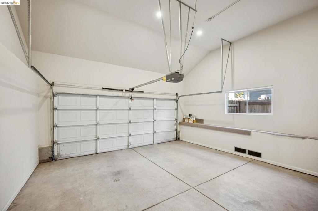 Garage space featuring high vaulted ceilings, a concrete floor, a white sectional garage door, and a horizontal window