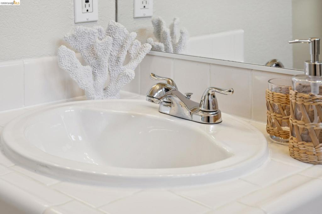 White tile countertop with integrated porcelain drop-in sink, chrome double-handle faucet, and full-width vanity mirror