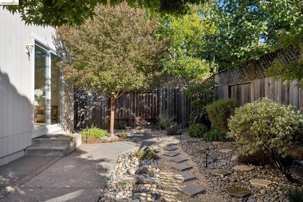 Private backyard featuring a concrete patio, stone garden path, decorative rock ground cover, and wood perimeter fencing with lattice top
