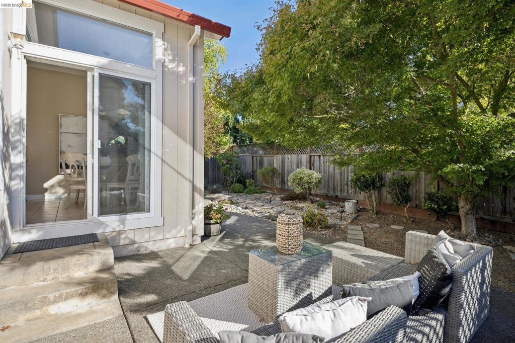 Concrete patio featuring a sliding glass door with a transom window, wood-finish privacy fencing, and mature landscape trees
