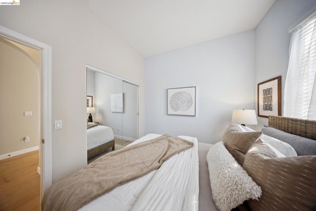 Interior room featuring wood-finish flooring, high ceilings, arched doorway, and a dual-panel mirrored sliding closet