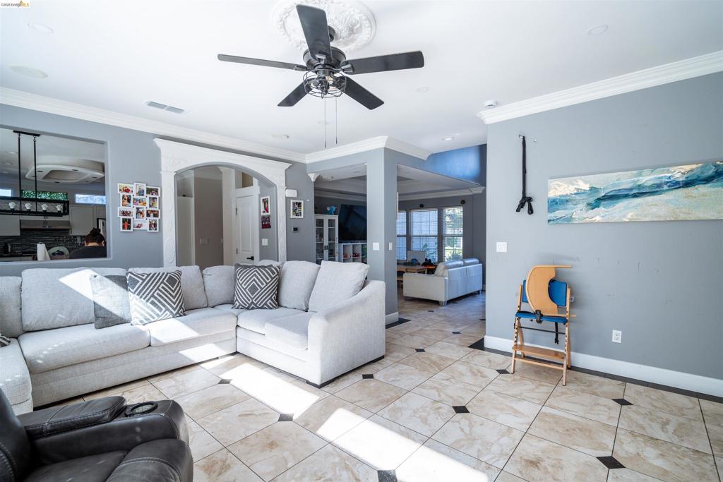 Living area featuring tile flooring with dark accent insets, crown molding, a central ceiling fan with a decorative medallion, and arched architectural detailing