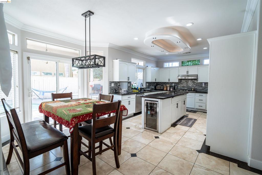 Kitchen featuring white cabinetry, dark stone countertops, an integrated beverage cooler, tile flooring with decorative inserts, and custom recessed ceiling lighting