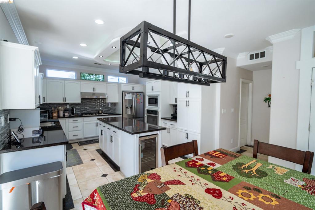 Kitchen featuring white shaker-style cabinetry, dark stone countertops, a central island with an integrated beverage refrigerator, geometric metal pendant lighting, and tiled flooring