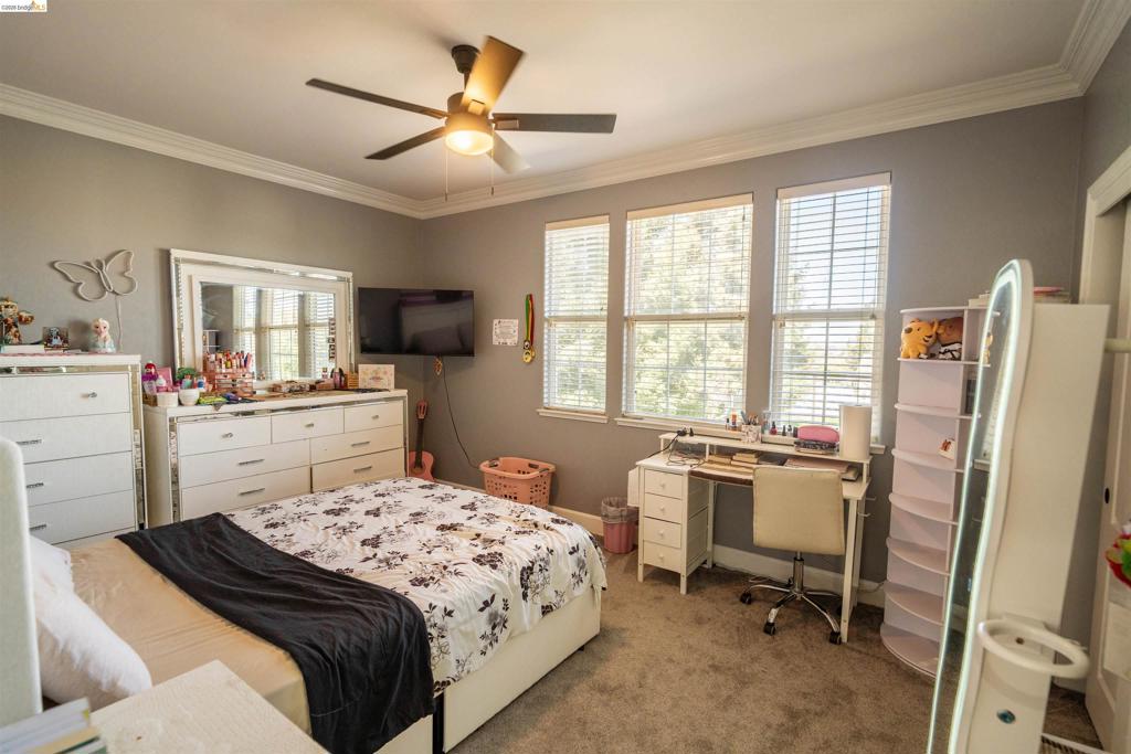 Bedroom featuring crown molding, neutral wall color, wall-to-wall carpeting, a multi-light ceiling fan, and triple-pane windows