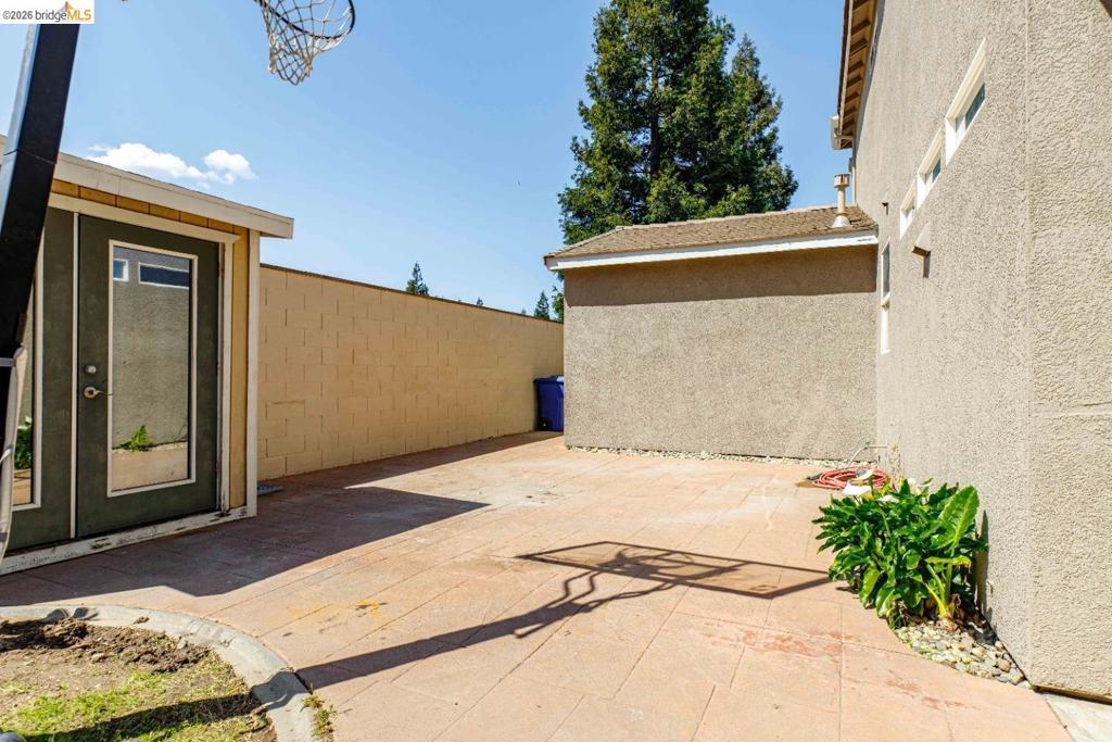 Side yard featuring concrete paver patio, stucco exterior walls, perimeter masonry wall, and mature coniferous trees