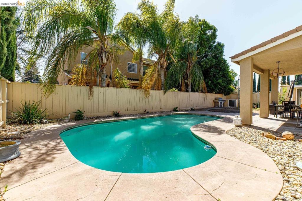 In-ground swimming pool featuring a curved concrete deck, covered patio, and perimeter privacy fencing