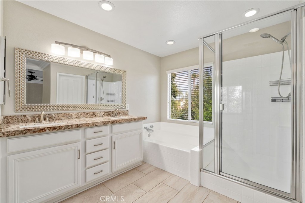 Another View Of The Primary Bathroom Showcasing The Beautiful Vanity, Soaking Tub Beneath A Large Window, Separate Glass-Enclosed Shower, And Abundant Natural Light.