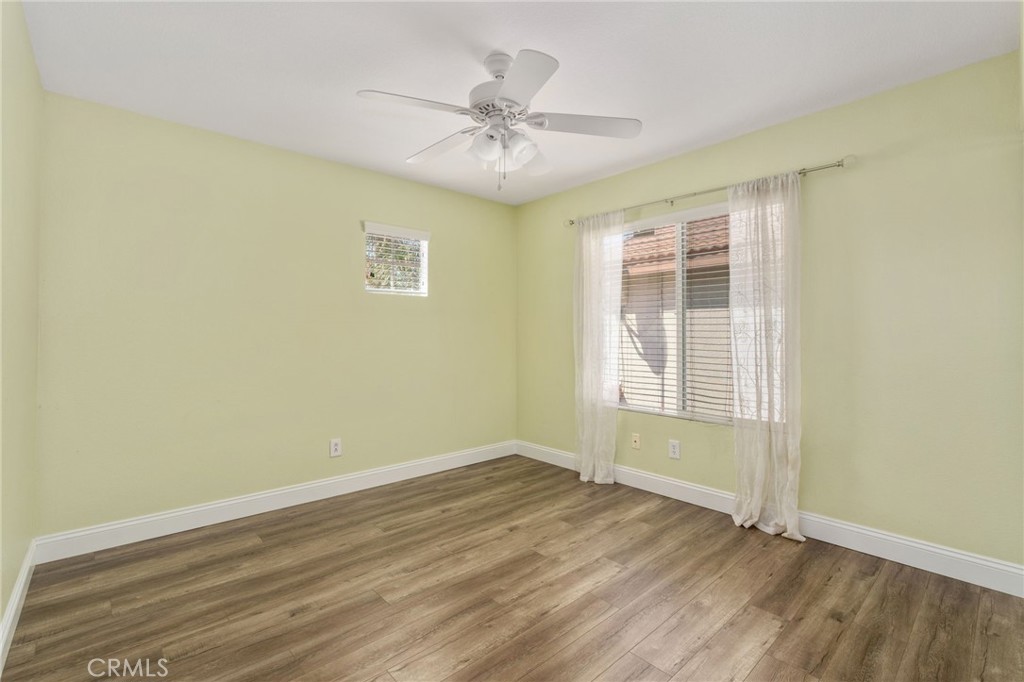 Bright And Inviting Bedroom Featuring Wood-Look Flooring, A Ceiling Fan, Soft Wall Colors, And A Large Window Allowing Plenty Of Natural Light.