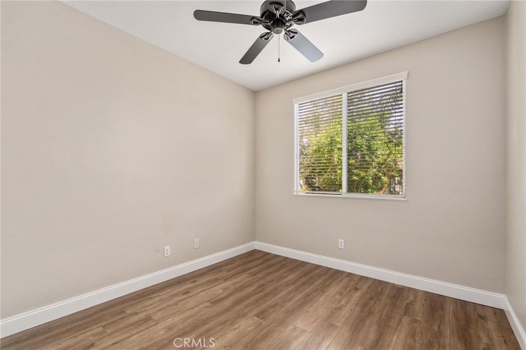Inviting Bedroom Featuring Wood-Look Flooring, A Ceiling Fan, Large Window Overlooking The Outdoors, And A Comfortable, Relaxing Atmosphere.