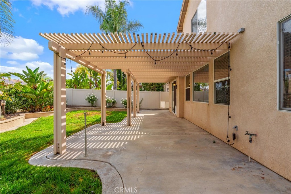 Spacious Pergola-Covered Patio Featuring An Inviting Outdoor Dining Area, Comfortable Seating, And Views Of The Beautifully Landscaped Backyard.