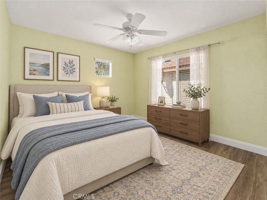 Bright And Inviting Bedroom Featuring Wood-Look Flooring, A Ceiling Fan, Soft Wall Colors, And A Large Window Allowing Plenty Of Natural Light. Digitally Staged