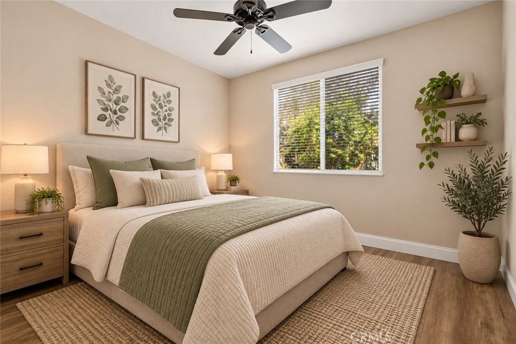 Inviting Bedroom Featuring Wood-Look Flooring, A Ceiling Fan, Large Window Overlooking The Outdoors, And A Comfortable, Relaxing Atmosphere. Digitally Staged