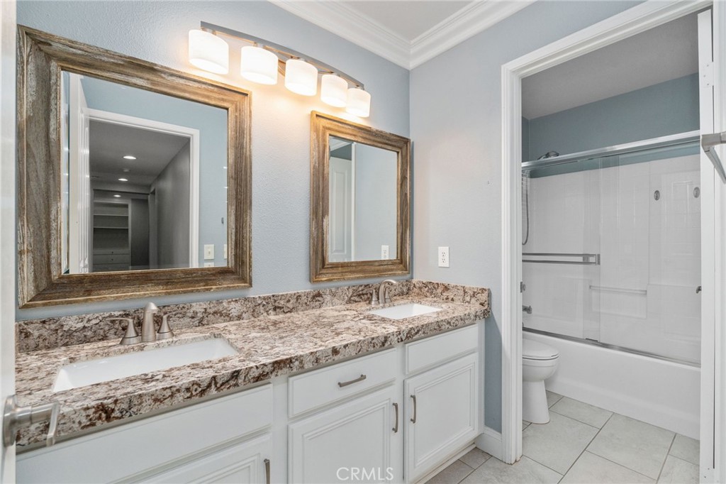 Spacious Secondary Bathroom Featuring Dual Sinks, Attractive Granite Countertops, Framed Mirrors, White Cabinetry, And A Tub And Shower Combination.
