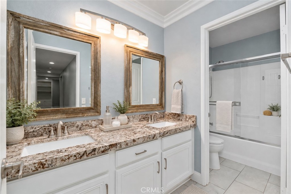 Spacious Secondary Bathroom Featuring Dual Sinks, Attractive Granite Countertops, Framed Mirrors, White Cabinetry, And A Tub And Shower Combination. Digitally Staged