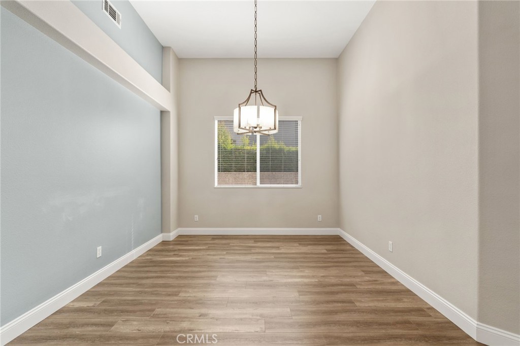 Elegant Formal Dining Room Featuring Soaring Ceilings, An Attractive Light Fixture, Wood-Look Flooring, And A Large Window Providing Natural Light.