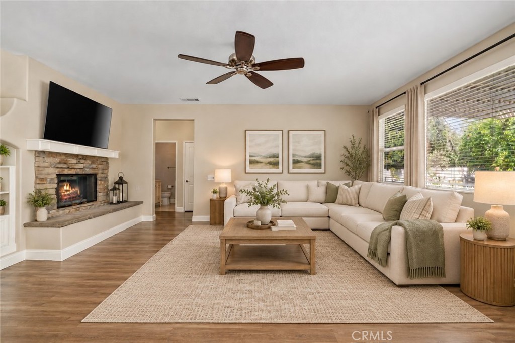 Another View Of The Spacious Family Room Highlighting The Beautiful Stone-Surround Fireplace, Wood-Look Flooring, Ceiling Fan, And Abundant Natural Light. Digitally Staged